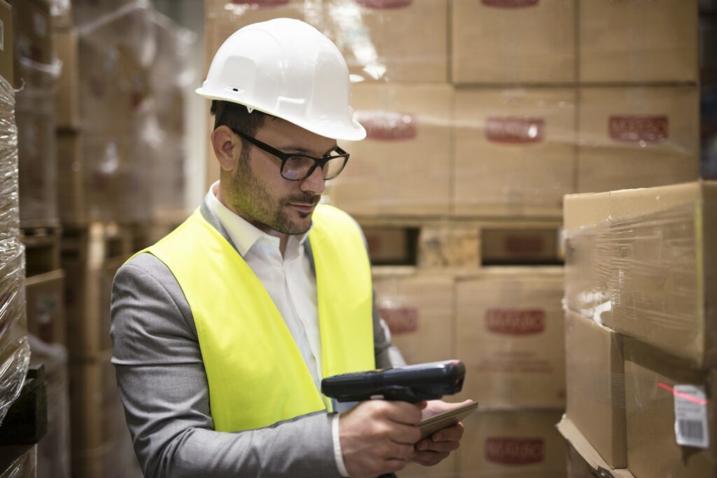 homme travaillant en logistique dans un entrepôt en train de scanner un code barre sur un carton.